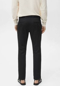 Pantaloni neri a slim fit, con una texture liscia, due tasche posteriori e una vita con passanti per la cintura, abbinati a sandali semplici.