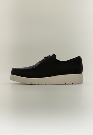 Chaussure en cuir noir à lacets avec une semelle blanche épaisse, montrée de profil sur un fond neutre.