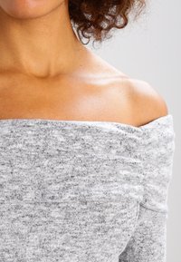 Top grigio a spalla scoperta con un design testurizzato a costine e dettagli di tessuto arricciato lungo il colletto e le maniche.