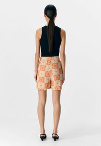 Top sin mangas negro combinado con pantalones cortos naranjas con un diseño estampado. Los pantalones cortos tienen un diseño texturizado con una cinturilla y llegan hasta la mitad del muslo.