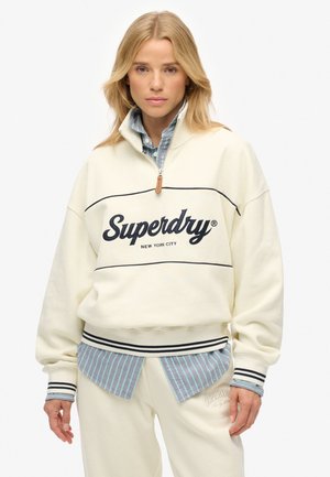 Pull en polaire écru avec col zippé, présente le logo "Superdry" en noir, des rayures horizontales et des poignets côtelés avec un tissu accent en dessous.