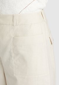 Beige linnen broek met een gladde textuur, voorzien van een platte tailleband en twee achterzakken. Minimalistisch ontwerp, geen zichtbare hardware.