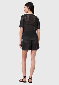 Zwart gebreid set met korte mouwen en shorts, met een open mesh-design, geribbelde zoom en platte sandalen. Gladde textuur en een ontspannen pasvorm.