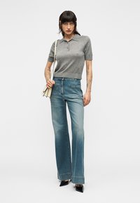 Polo gris en laine à manches courtes, associé à un jean bleu délavé taille haute et des escarpins noirs à bouts pointus. Sac à main beige minimaliste.