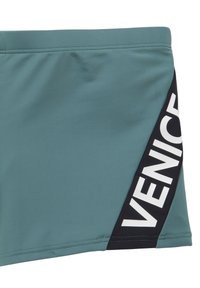 Tyrkysové plavky vyrobené z hladkej tkaniny. Obsahujú čierny bočný panel s bielym textom "VENICE", švíkové detaily a klasický strih.