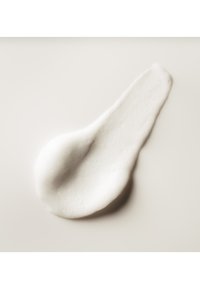 Wit romig cosmetisch product uitgespreid op een glad, licht beige oppervlak met een licht glanzende textuur.