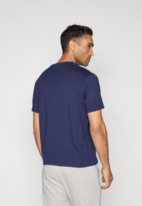 Navy blue short-sleeve t-shirt with a round neck, made of soft fabric, worn with light grey sweatpants, viewed from the back.