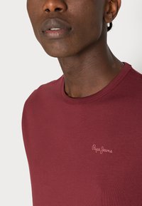 Bordeauxkleurig t-shirt met korte mouwen, voorzien van een ronde halslijn en een klein, lichtgekleurde "Pepe Jeans" logo op de borst.