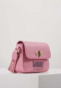 Rosa faux læder taske med klaplukning, guldfarvede detaljer og et logo; har en justerbar rem med tekstdesign.