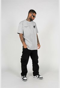 Grå bomuld t-shirt med brystlomme, parret med løstsiddende sorte cargo bukser med sidelommer og sort-hvide sneakers.