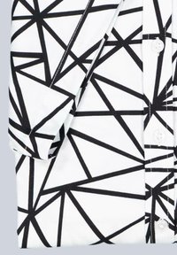 Weißes Hemd mit einem schwarzen geometrischen Muster, das aus kantigen Linien besteht. Der Stoff ist glatt, mit sichtbaren Knöpfen und einem umgeschlagenen Ärmel.