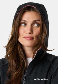 Black zip-up hoodie with a pink inner lining, featuring a logo on the chest and a close-fitting hood. Soft texture and sporty design.