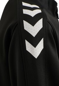 Zwarte sportjas met een gestructureerde stof en witte chevronpatronen op de schouders. Glad afwerking, sportief ontwerp, aansluitende silhouet.