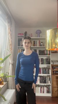 Blauw geribbeld langbrengs T-shirt met een ronde hals, gecombineerd met zwarte broek. Achtergrond met boekenkasten en een decoratieve lamp.