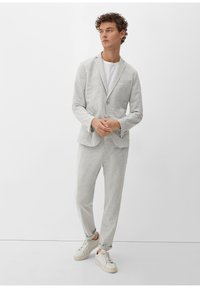 Lichtgrijs, zacht geweven pak met een blazer met één knoop en bijpassende taps toelopende broek, gecombineerd met witte sneakers en een eenvoudig wit T-shirt.