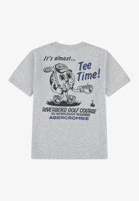 Γκρι βαμβακερό μπλουζάκι με σχέδιο κινουμένων σχεδίων που απεικονίζει μια μπάλα γκολφ να κρατάει ρόπαλο γκολφ και κύπελλο, με navy μπλε κείμενο και γραφικά στην πλάτη.