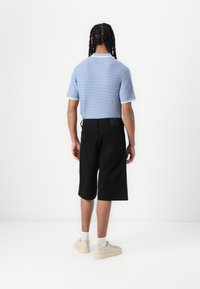 Blue knit polo shirt with short sleeves, black knee-length shorts, white accents, paired with cream sneakers and white socks.