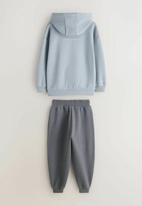 Light blue hoodie with hood, cuffs, and logo detail on the back, paired with gray elastic-waist joggers. Smooth fabric, casual fit.