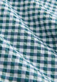 Groen en wit geblokt stof met kleine vierkantjes, voorzien van een gestructureerd oppervlak en een zacht geweven patroon. Geschikt voor kleding of woningdecoratie.