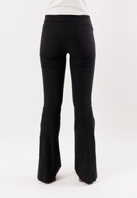 Pantaloni neri a zampa d'elefante con vita alta, realizzati in un tessuto liscio e elastico. Presentano una silhouette aderente con gamba leggermente svasata.