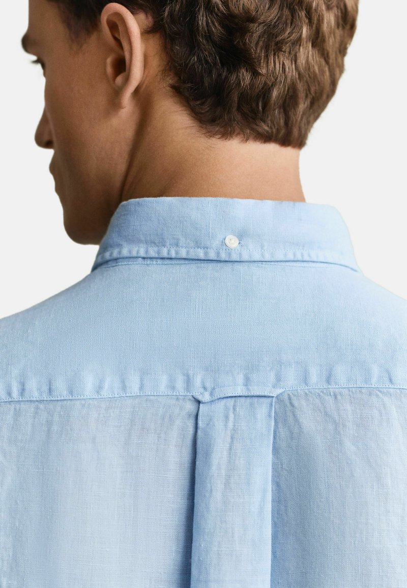 Mann trägt hellblaues Hemd mit Knöpfen, zeigt den Nacken und oberen Rücken mit natürlichem Haar- und Hautton.