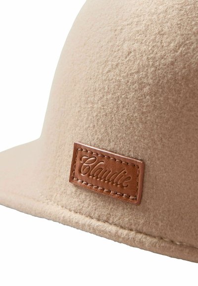 Sombrero beige de fieltro con parche de cuero marrón cosido con la etiqueta "Claudie" en el lado frontal.