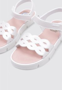 Sandalias blancas con un diseño de tira trenzada, una plantilla suave en color rosa y una suela blanca acolchada. Correa ajustable en el tobillo para un ajuste seguro.