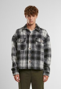 Svart og hvit rutete flanellskjorte med knappeåpning, to brystlommer og krage. Myk tekstur med en avslappet passform.