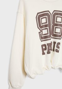 Felpa crema con scollo rotondo, vestibilità over size e maniche lunghe, caratterizzata da un testo grafico marrone scuro "98 PARIS" sul davanti.