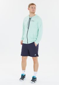 Lyse mintfarvet zip-up hoodie med en frontlomme, parret med marineblå shorts. Skoene er grå med blå accenter, og hvide sportssokker.