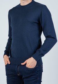 Marineblauer Strickpullover mit Rundhalsausschnitt, langen Ärmeln und gerippten Bündchen. Der Stoff wirkt glatt; taillierte Passform und minimalistische Details.