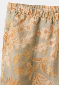 Tissu avec motif floral beige et orange clair et taille élastique, montrant des motifs détaillés de feuilles et de fleurs.
