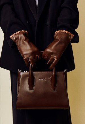 Braune Lederhandtasche mit strukturierter Form, ausgestattet mit zwei Griffen. Die Trägerin trägt passende braune Lederhandschuhe mit Leopardenmuster-Akzenten.