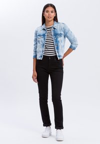 Jasnoniebieska kurtka dżinsowa z przecieranymi akcentami, połączona z czarno-białą koszulą w paski, czarnymi spodniami slim fit i białymi sneakersami.