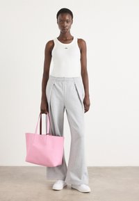 Hvit tank topp med grønt logo, grå plisserte sweatpants, rosa tote bag med mørke håndtak, og hvite sneakers; glatte teksturer og avslappet passform.