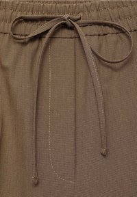 Tissu marron à motif avec une texture douce. Comprend une taille élastique et un lien à l'avant. Remarquable pour son design à petits carreaux fins et ses coutures.