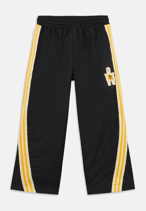 Schwarze Sporthose mit einem elastischen Bund, gelben seitlichen Streifen und einem strukturierten Smiley-Patch auf der Vorderseite. Weiches, leichtes Material.