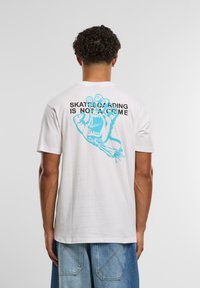 Hvit bomulls t-skjorte med en blå grafikk av en hånd som skriker, og tekst som sier "SKATEBOARDING ER IKKE EN KRIIM" på baksiden.