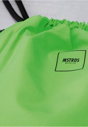 Lysegrøn snørepose med sorte snore og et sort firkantet logo med teksten "MSTRDS Munich" på stoffet.