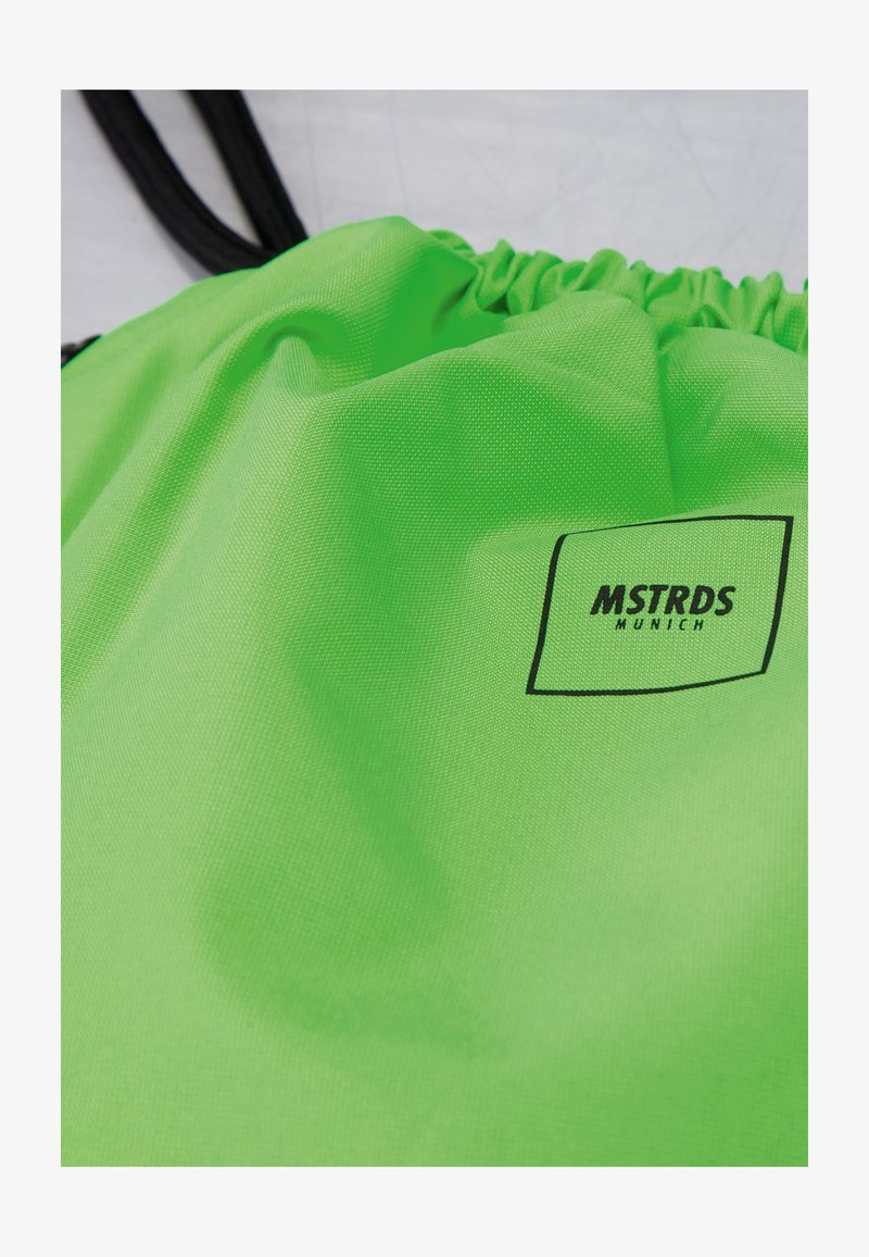 Sac à cordon vert vif avec cordons noirs et un logo carré noir indiquant "MSTRDS Munich" sur le tissu.