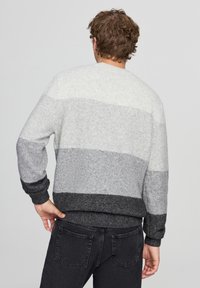 Maglione a righe grigie e nere in una morbida maglia, con scollo rotondo e polsini e orlo a costine, indossato di spalle.