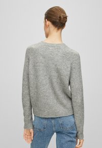 Grå ulltröja med mjuk textur, ribbad nederkant och ärmslut. Har en rundad halslinning och en liten logotypdetalj på baksidan.