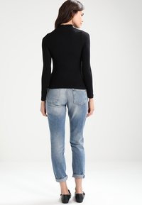 Musta pitkähihaisen paita, joka on yhdistetty vaaleansinisiin käärittyihin farkkuihin, joissa on slim fit -leikkaus ja tavalliset taskut, taustalla yksinkertainen tausta.