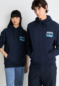 Les sweat-shirts navy sont dotés de poches frontales, de cordons de serrage réglables et d'un logo coloré. Tissu doux avec une coupe décontractée.