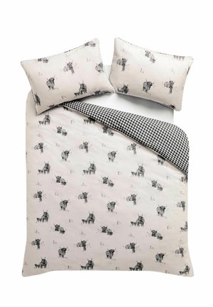 Funda nórdica blanca y almohadas con ilustraciones de vacas en blanco y negro, una esquina doblada revela un patrón de cuadros en blanco y negro debajo.