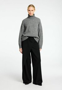 Pull en laine gris à col roulé avec ourlet côtelé, porté avec un pantalon noir à taille haute et à jambes larges avec une superposition frontale asymétrique.