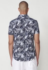 Kratkoročna srajca temno modre barve z belim tropskim listnim vzorcem. Tkanina iz bombažne mešanice, standardni ovratnik in ukrivljen rob.