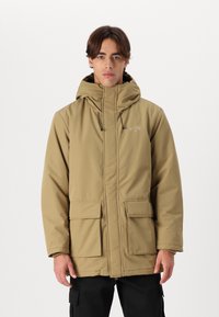 Khaki gewatteerde jas met een vooraanlopende rits en verstelbare toggles. Beschikt over twee voorkruiden en een licht gestructureerd oppervlak.