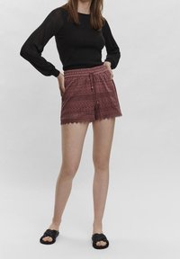 Burgundské krajkové šortky s vlnitým lemem a elastickým pasem. V kombinaci s černým topem s dlouhým rukávem a černými nazouvacími sandály.