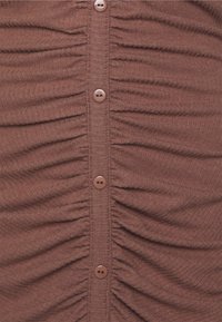 Top castanho em tecido canelado com franzido vertical e seis botões redondos na frente. Textura suave, material macio.